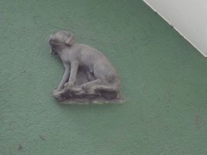 Eine steinerne Figur eines Hundes an grüner Mauer